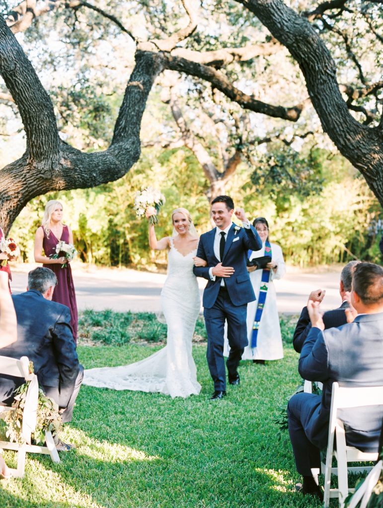 Film Fall wedding in Austin, Texas. Groom is wearing a navy suit, bride is wearing a lace wedding dress. Walking down the aisle as husband and wife.