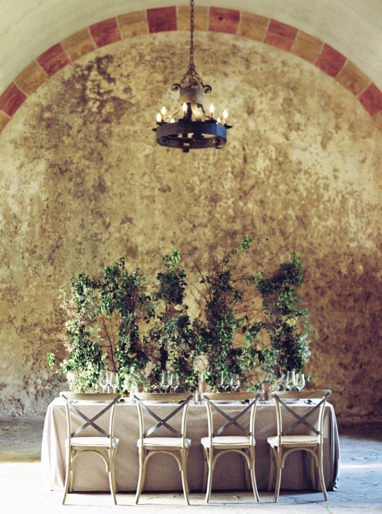 Mission San Jose head table with greenery hanging from above and wooden reception chairs.